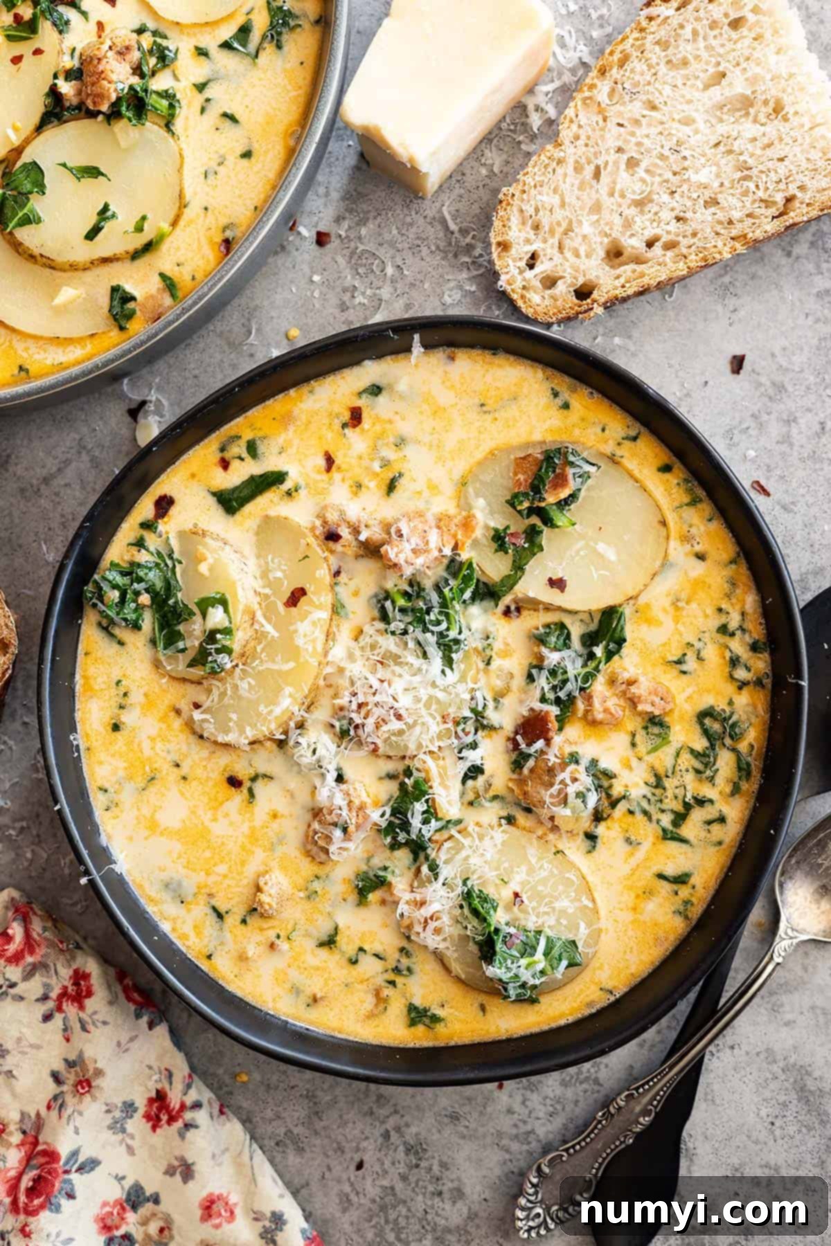 Overhead view of a bowl of soup. A chunk of parmesan off to the side along with slices of bread.