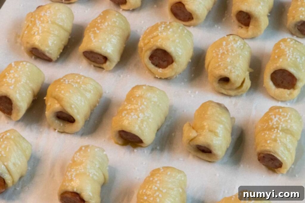 unbaked sausage pretzel bites with egg wash and pretzel salt on a cooking sheet