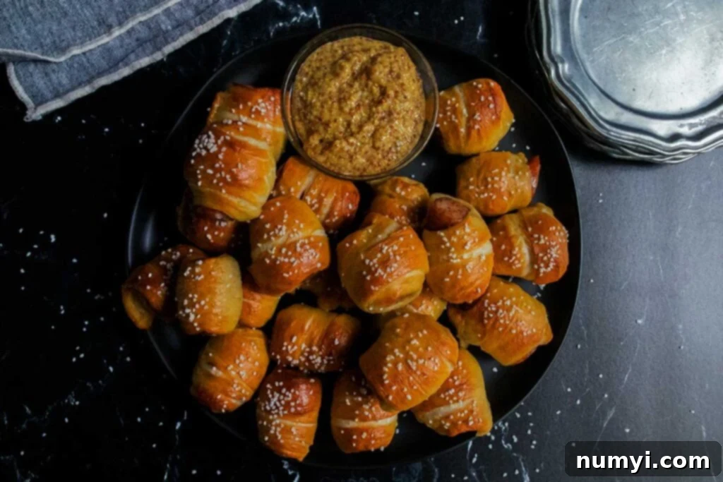 Sausage pretzel bites on a black plate with stone ground mustard garnish