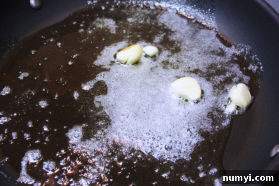 Cracked garlic cloves gently sautéing in a mixture of olive oil and melted butter in a hot skillet, releasing their fragrant aroma.
