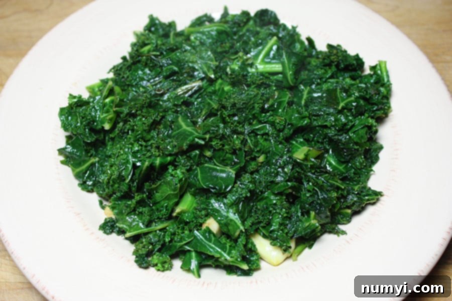 A vibrant green pile of freshly sautéed kale, perfectly cooked and seasoned, rests on a white plate with a subtle garnish, ready to be enjoyed as a healthy and flavorful side dish.