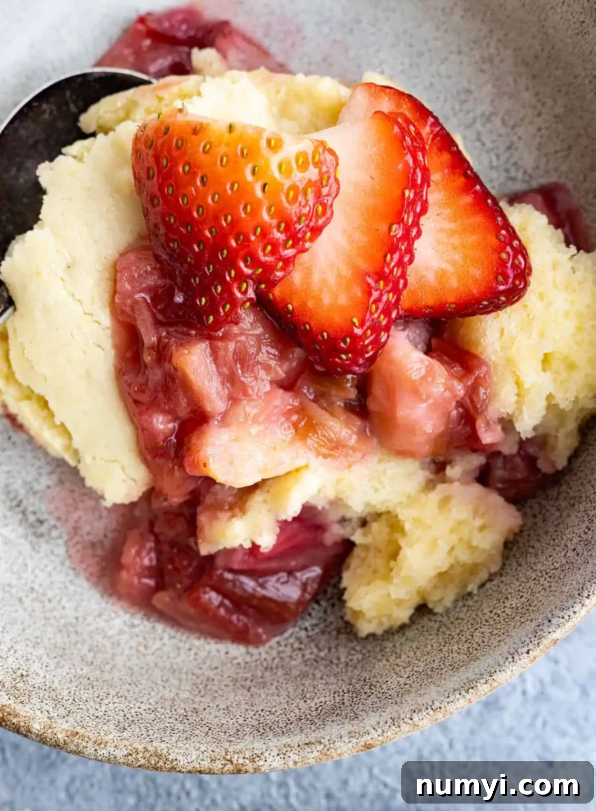 Overhead view of strawberry rhubarb pudding cake in a bowl. Fresh strawberries on top.
