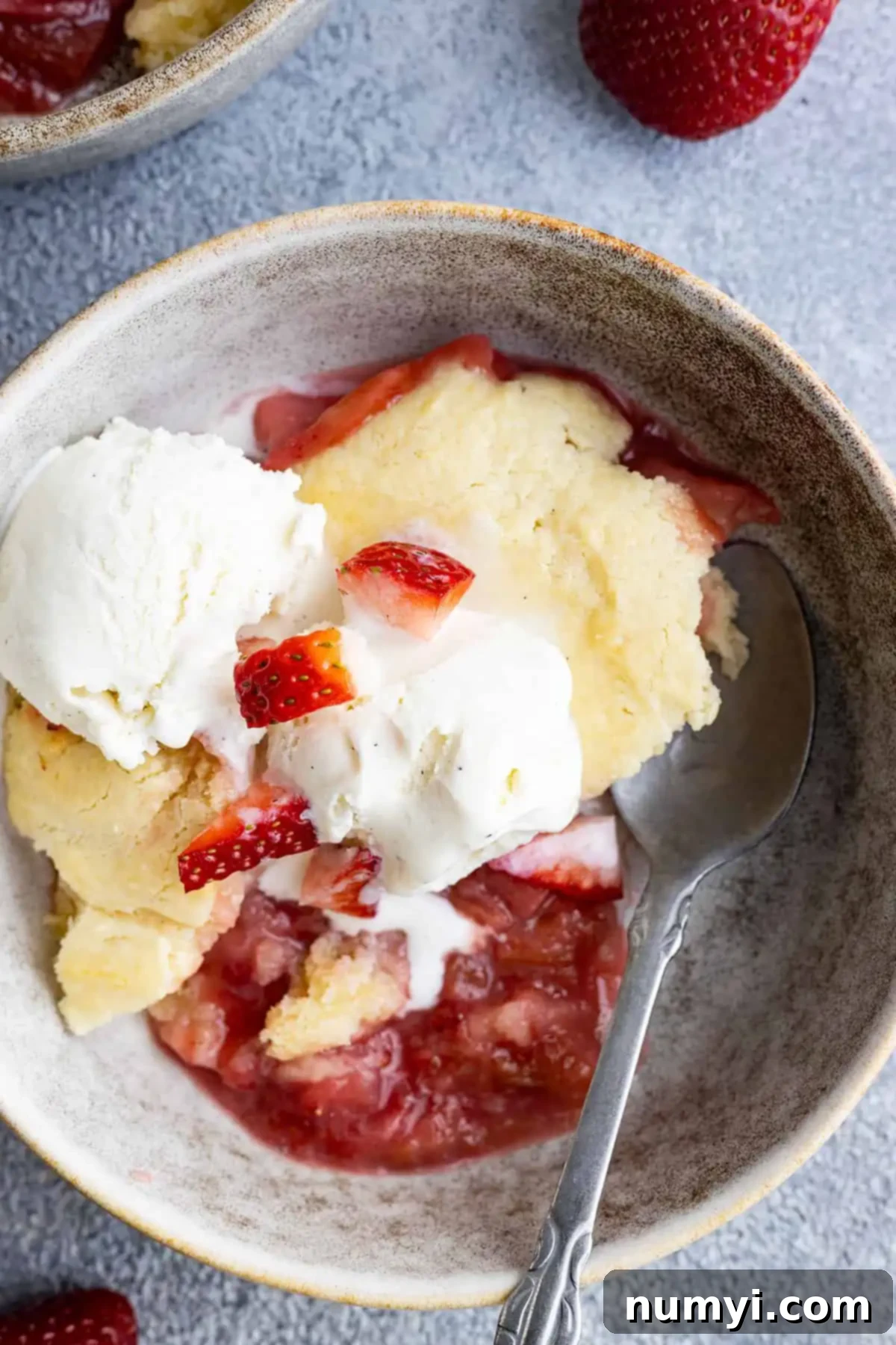 Overhead view of cake in a bowl with ice cream and a spoon. 