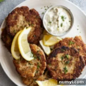Overhead view of tuna patties on a white platter with tarter sauce and lemon wedges.