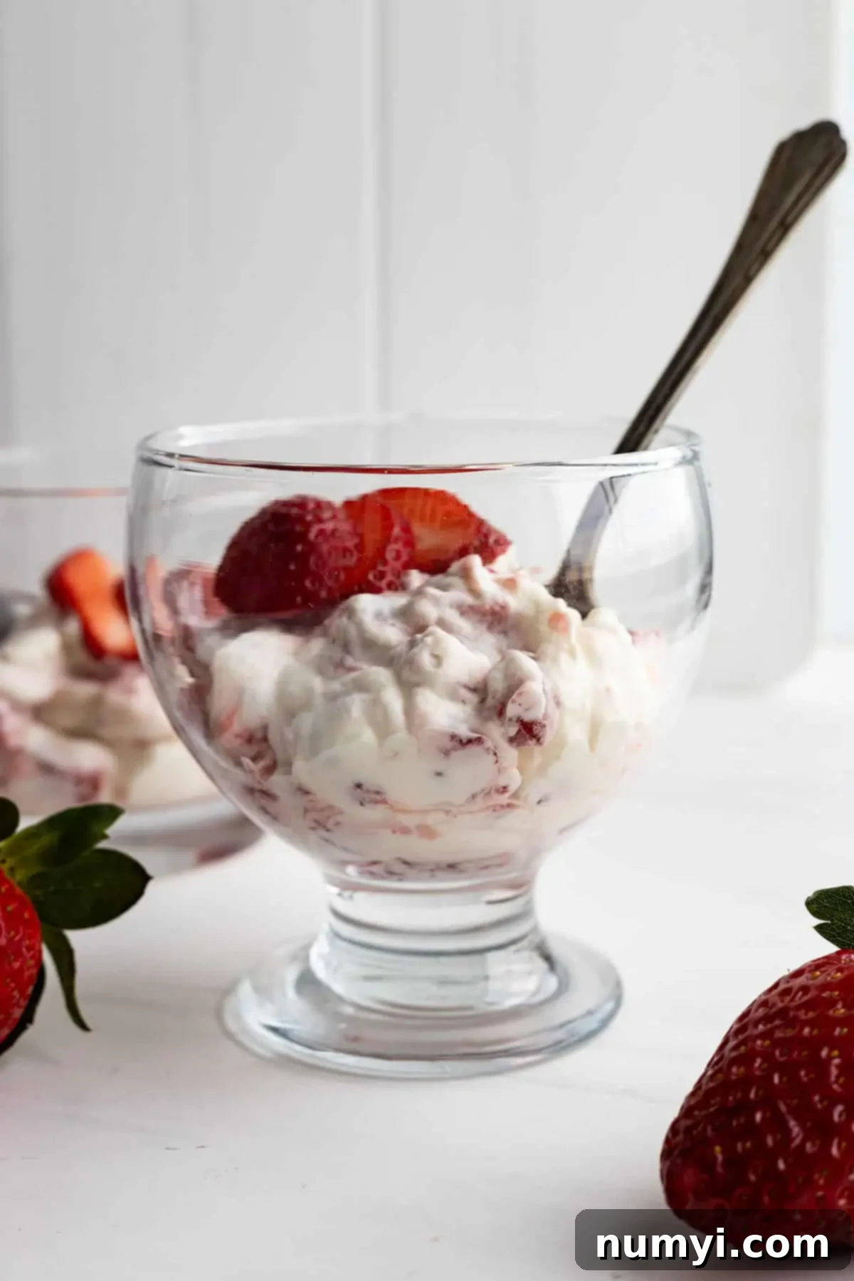 A close-up shot of a single serving of Strawberry Rhubarb Fool in a glass cup, adorned with fresh strawberry slices and a spoon, ready to be enjoyed.