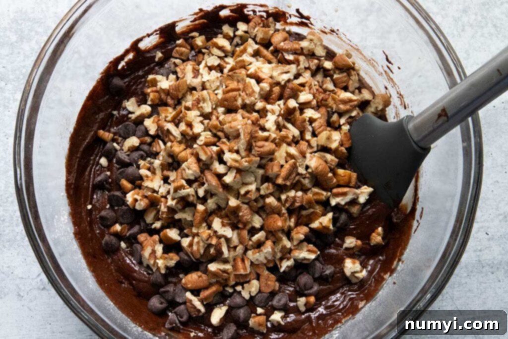 Brownie cookie batter being mixed in a large glass bowl with an electric mixer.
