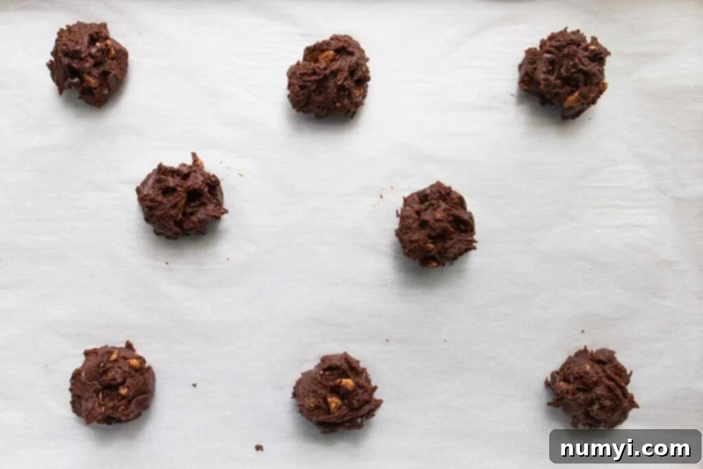Portioned brownie cookie dough balls arranged on a parchment-lined baking sheet, ready for baking.