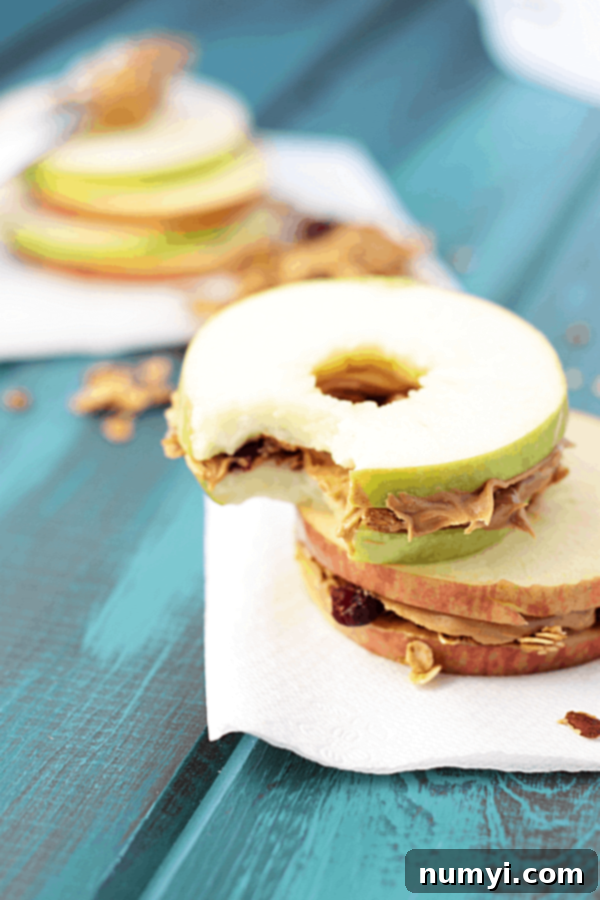 apple and peanut butter sandwiching granola on a blue wooden surface