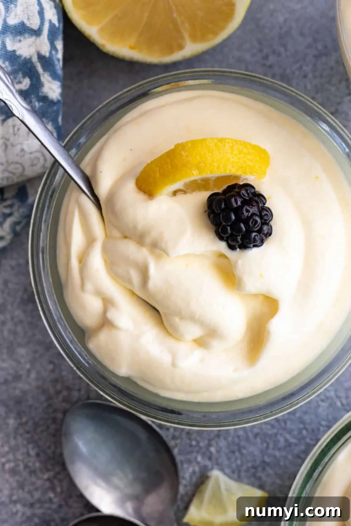 Overhead view of lemon mousse garnished a blackberry and lemon slice. Spoon in the mousse. 