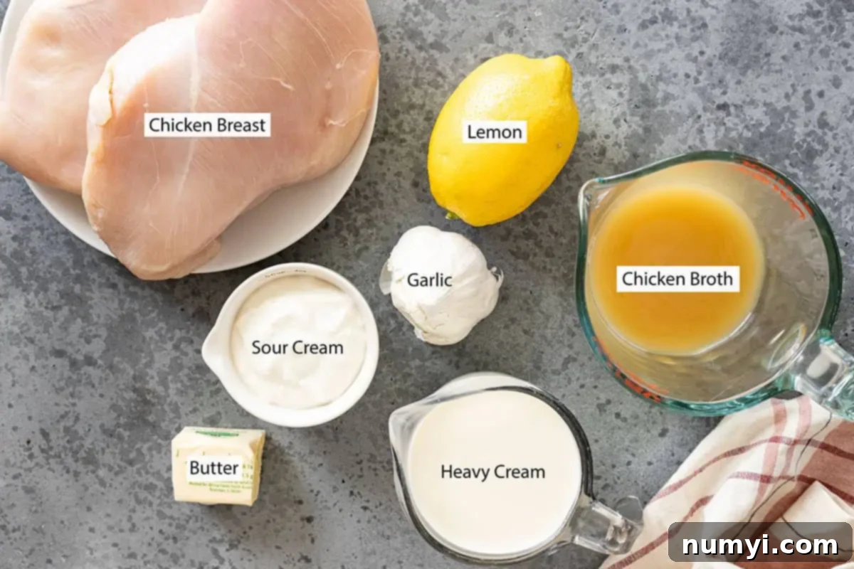 Ingredients: Chicken breast, lemon, chicken broth, garlic, sour cream, butter, heavy cream. All laid out on a wooden board.