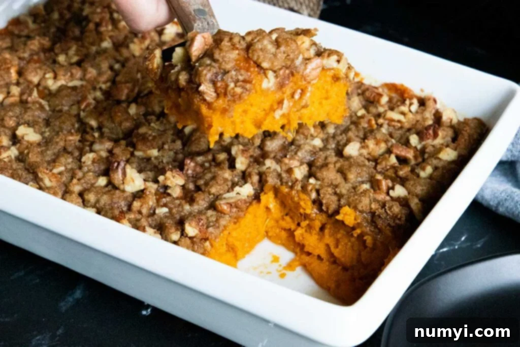 A perfectly baked slice of sweet potato casserole being served from a white baking dish.