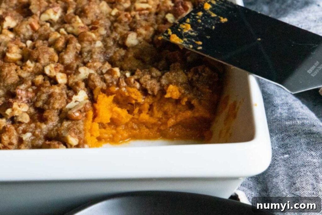 Close-up of baked sweet potato casserole with golden pecan topping in a white baking dish.