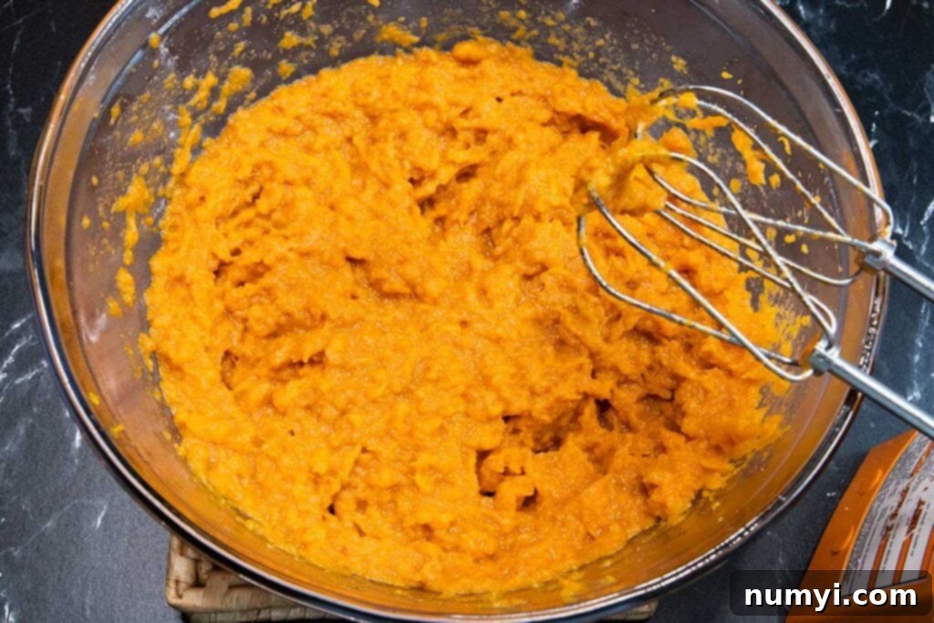 Mashed sweet potatoes in a large glass mixing bowl, perfectly smooth.