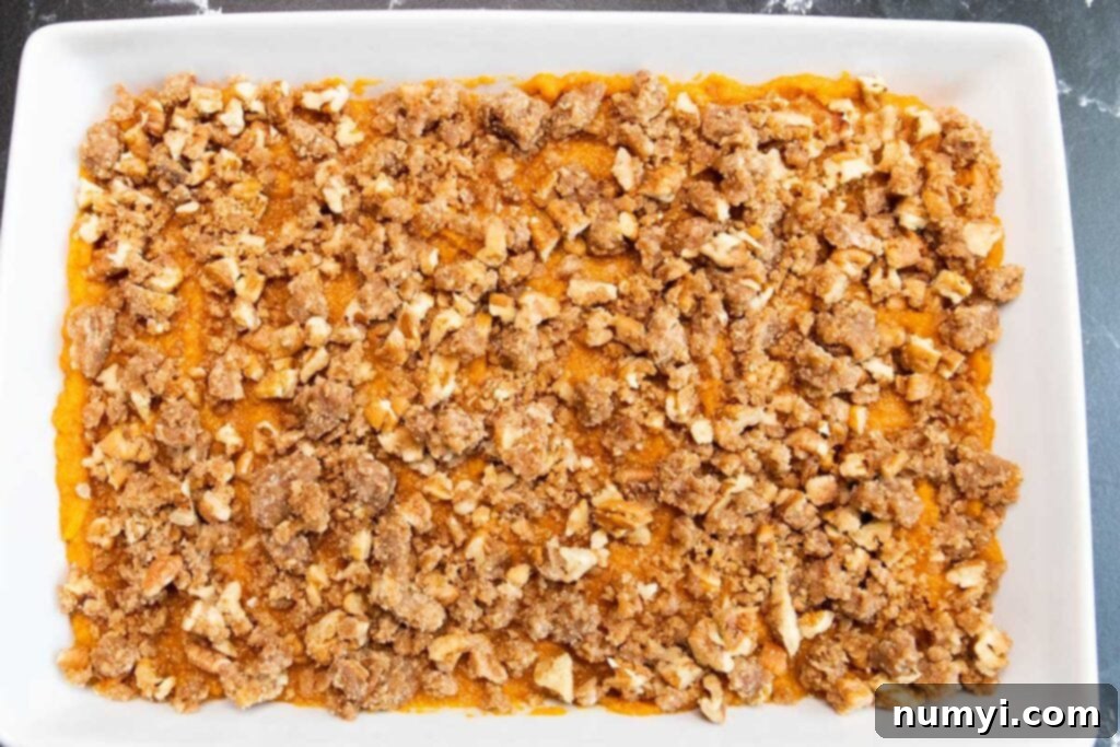 Unbaked sweet potato casserole with pecan topping spread evenly in a white baking pan, ready for the oven.
