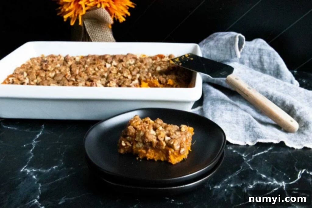 A generous serving of sweet potato casserole on a black plate, garnished with a sprig of rosemary.