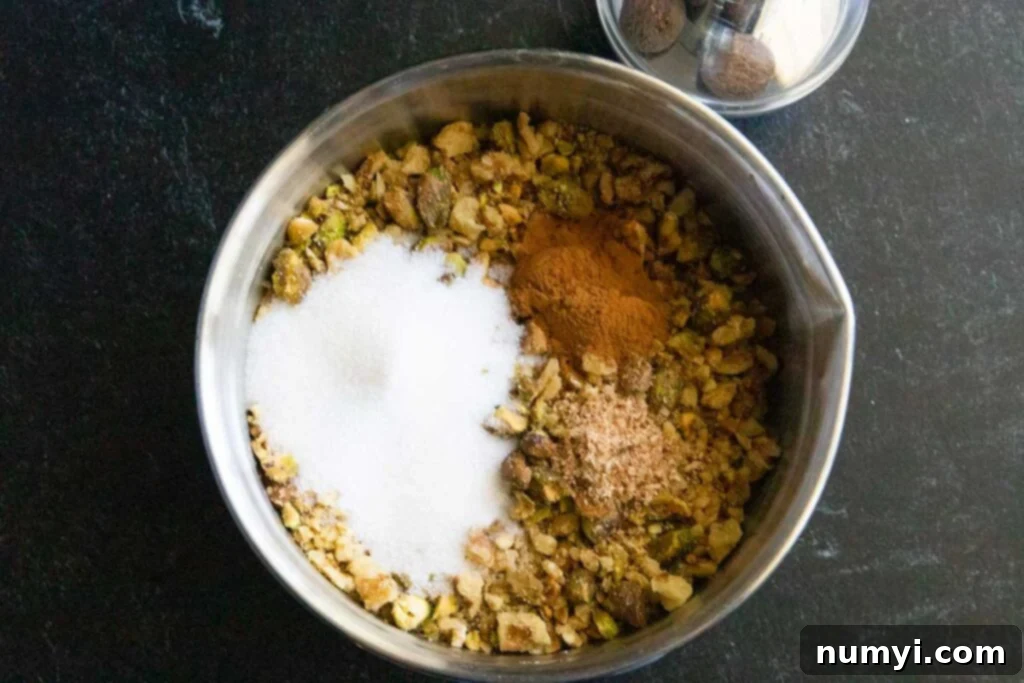 Coarsely chopped walnut and pistachio nut mixture in a metal bowl, seasoned with sugar and spices.