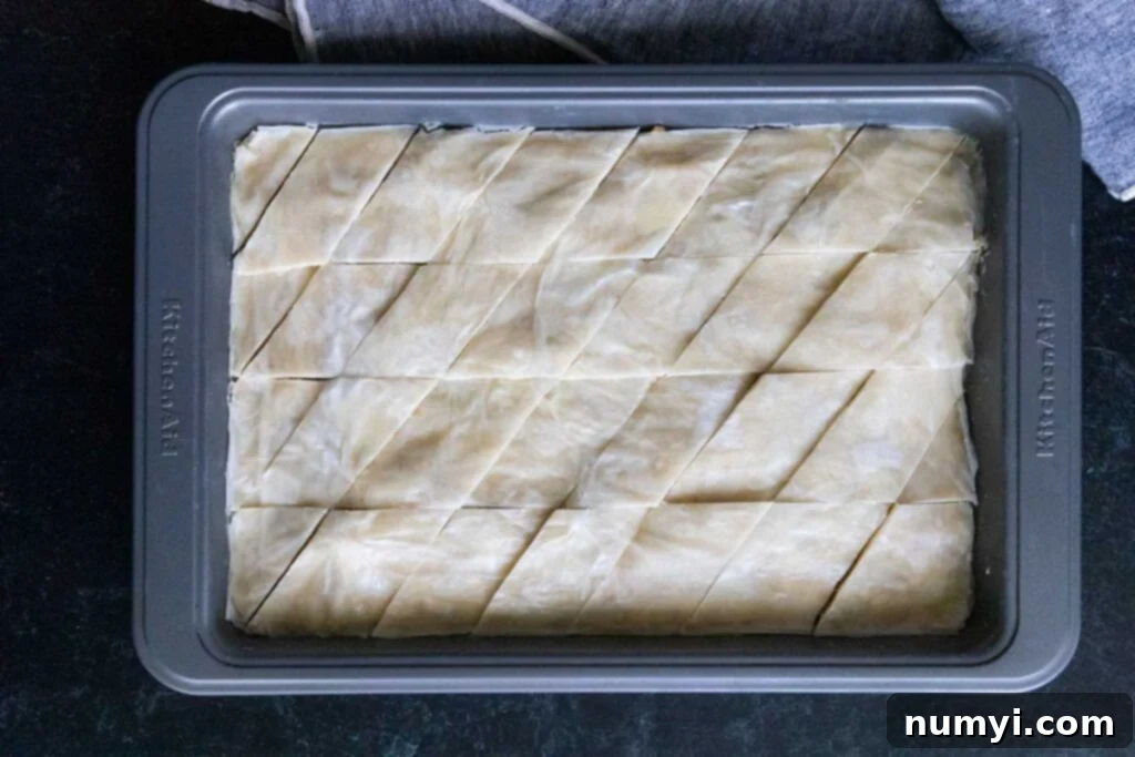 Diamond-shaped cuts scored into the baklava pastry in a baking pan before baking, ensuring even syrup distribution.
