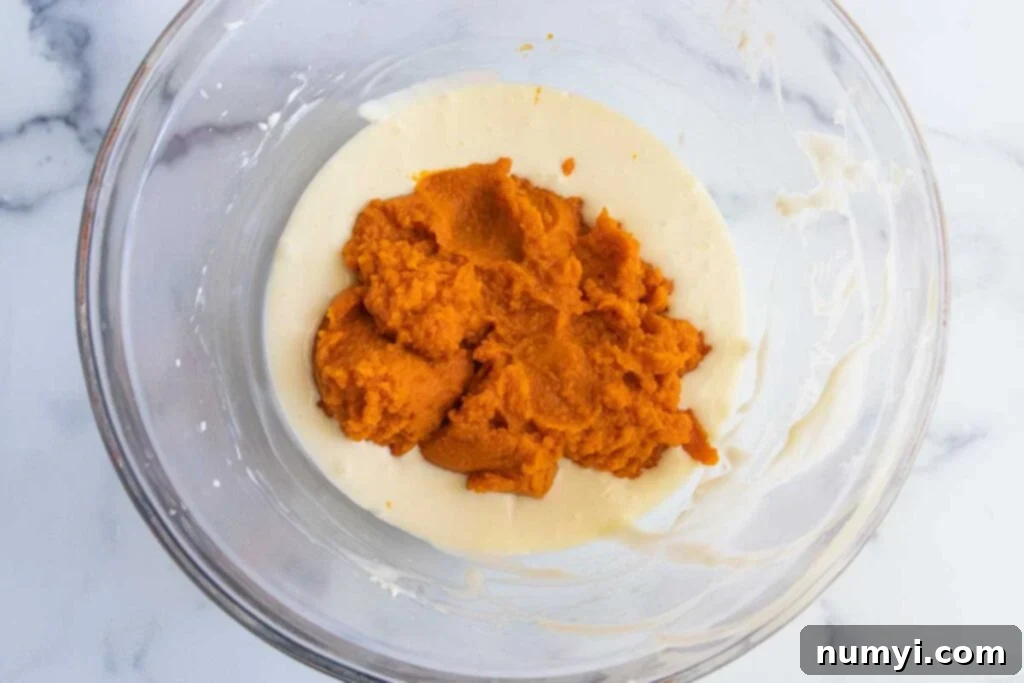 Cheesecake batter mixed with vibrant orange pumpkin puree in a glass bowl, creating the pumpkin layer for the bars.