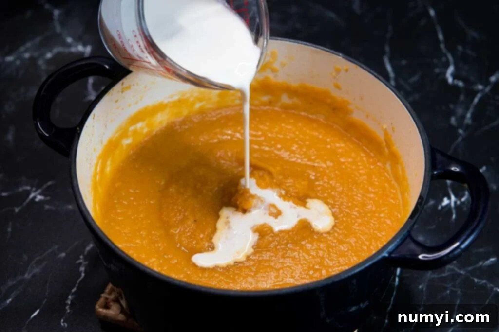 Rustic Root Medley 8 Heavy cream being poured into the pureed root vegetable soup in a pot.