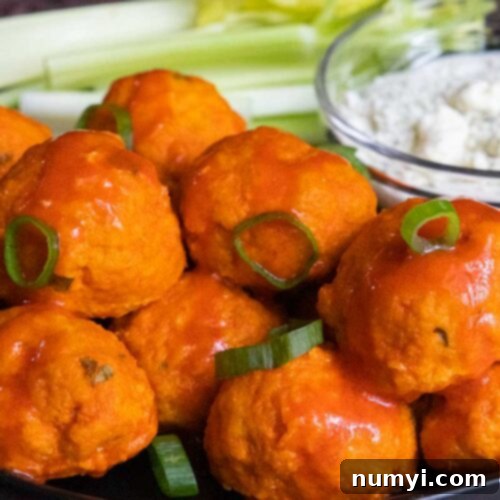 Buffalo chicken meatballs with celery and blue cheese on a black plate.