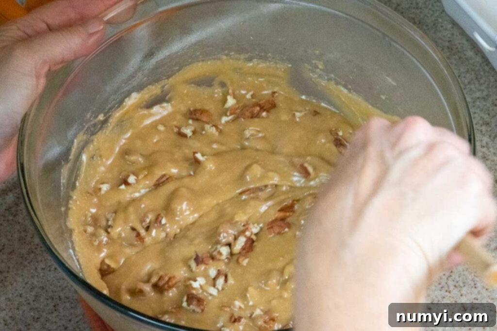 Toasted pecan pieces being stirred into the creamy fudge mixture.