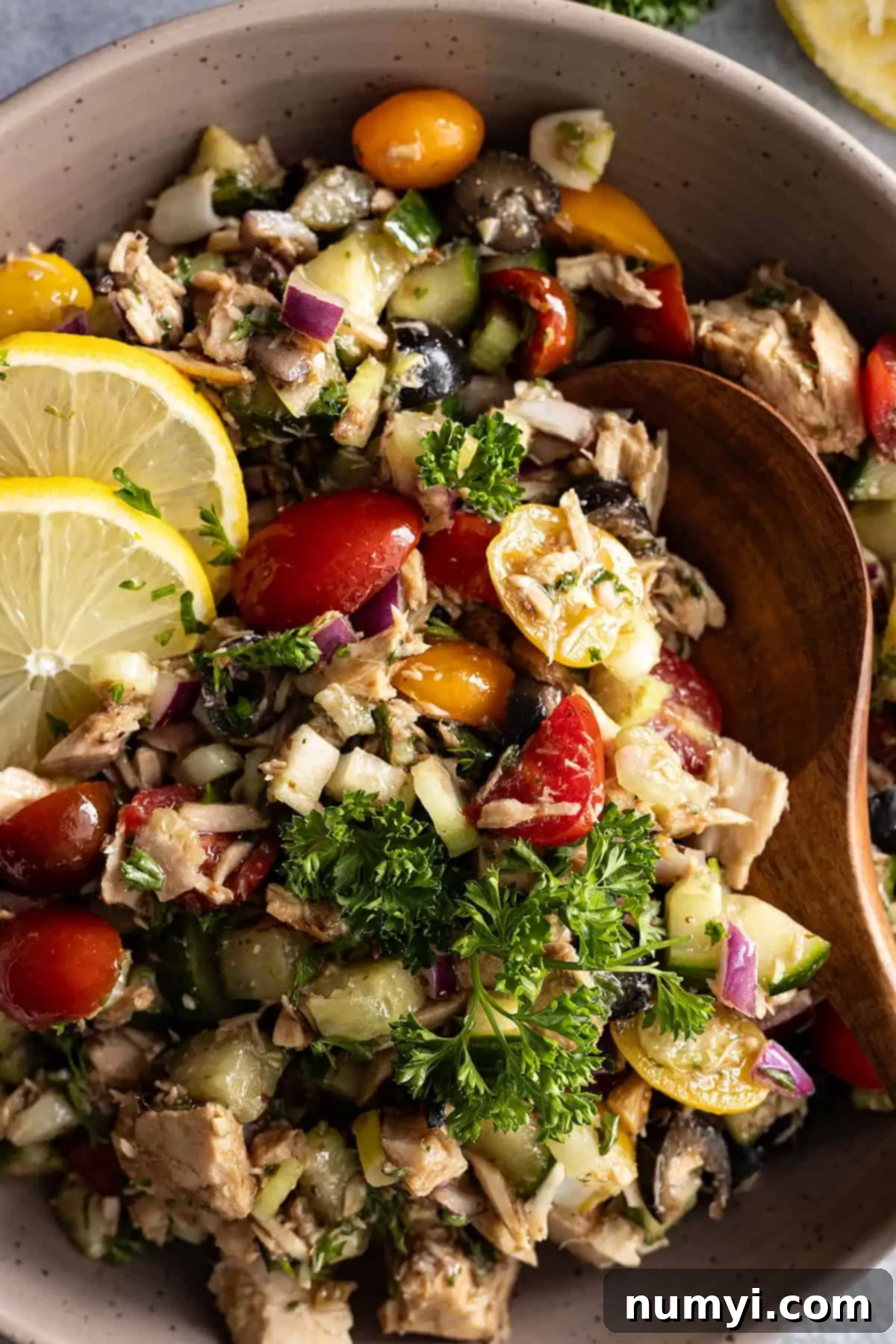 A spoon dipping into the Mediterranean tuna salad, garnished with fresh dill and lemon wedges, ready to serve.
