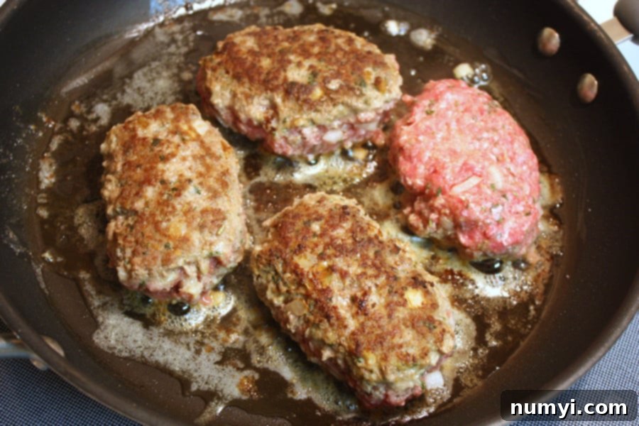 Homestyle Salisbury Steak with Rich Mushroom Gravy 2 Salisbury steak patties cooking in a skillet, sizzling and browning perfectly.