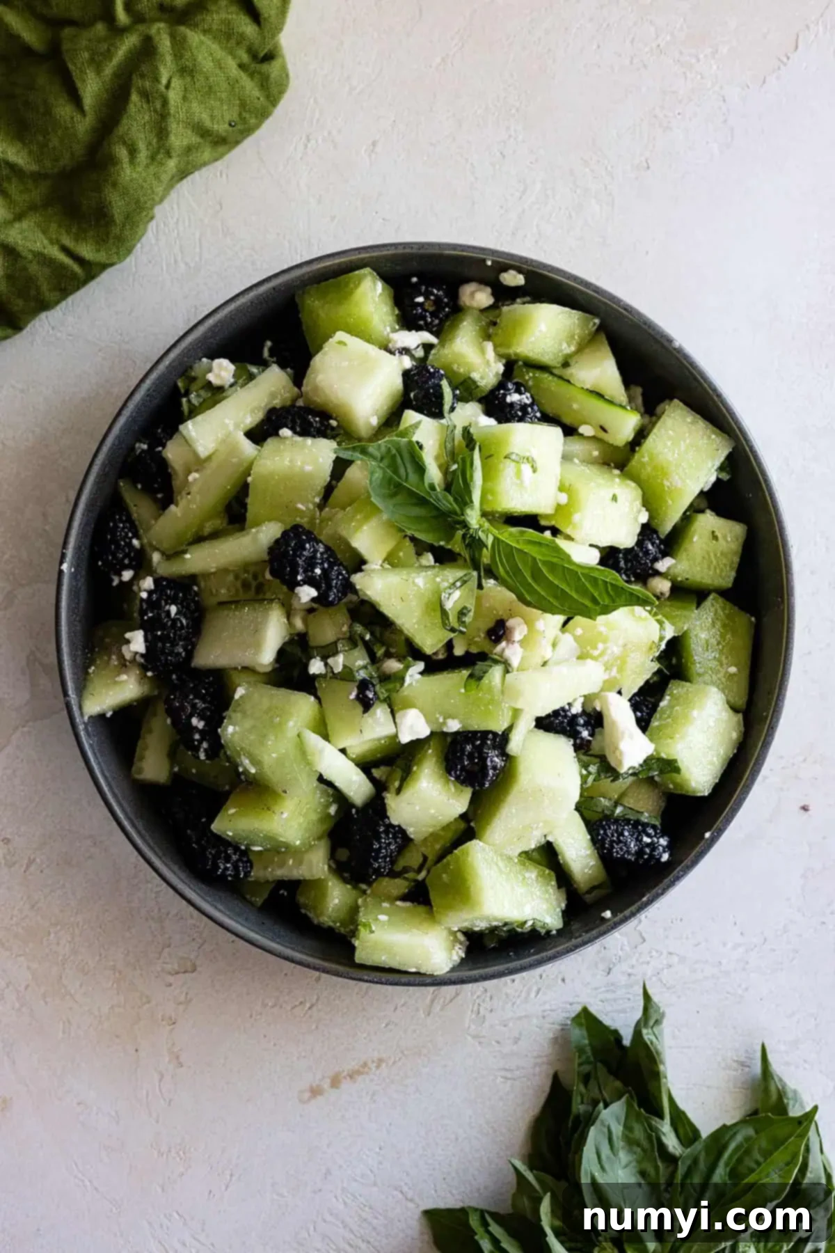 Crisp Honeydew Cucumber Medley 2 Overhead view of cucumber honeydew salad in a bowl with basil off to the side.