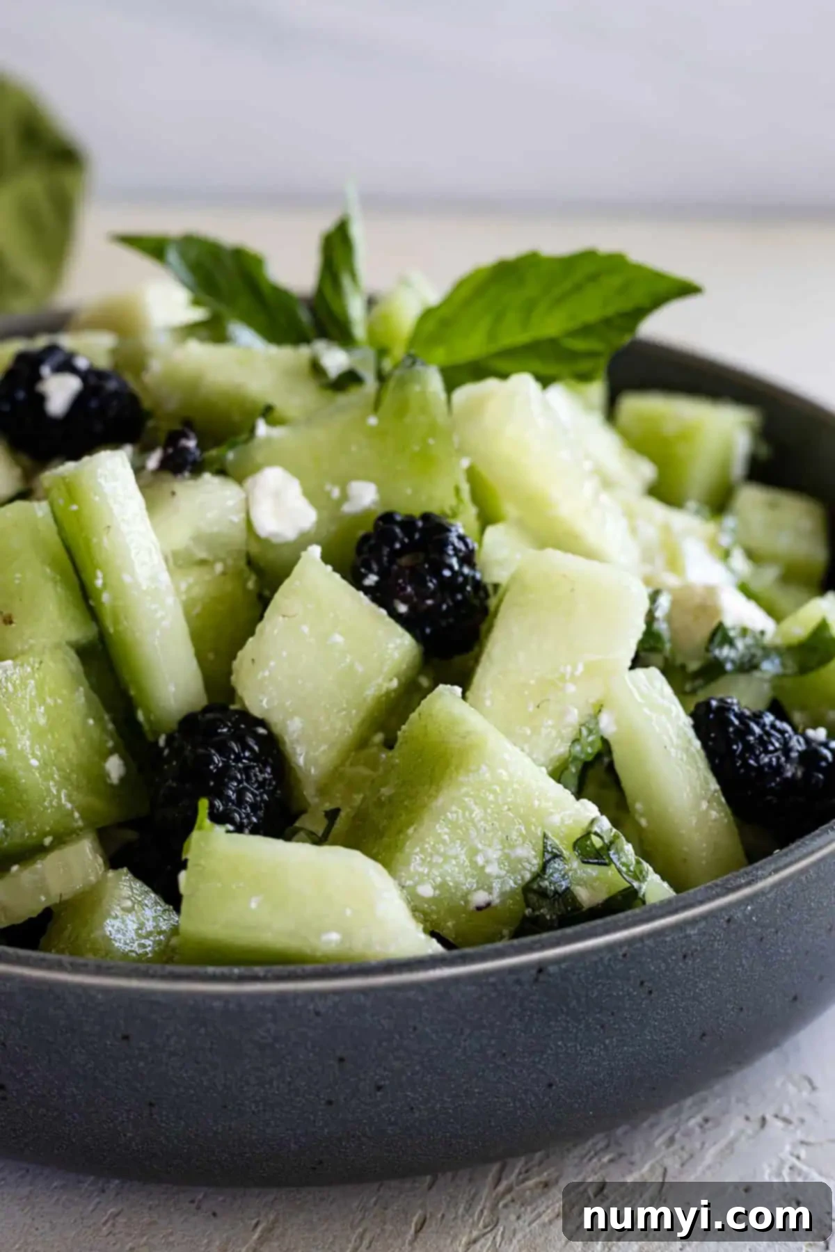 Crisp Honeydew Cucumber Medley 5 Side view of salad in a blue bowl with a sprig of basil for garnish.
