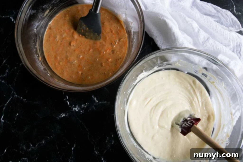 Two glass mixing bowls, one containing a smooth, pale cheesecake batter and the other a rich, orange-hued carrot cake batter, ready for layering.