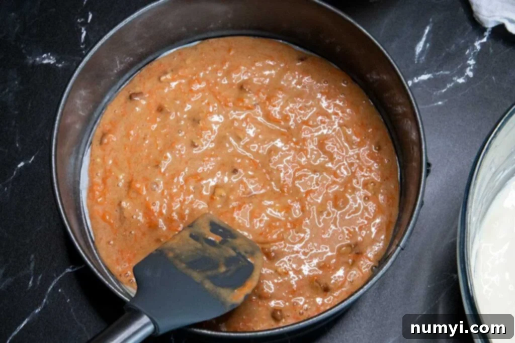 The first layer of moist carrot cake batter spread evenly at the bottom of a 9-inch springform pan, ready for the next layer.