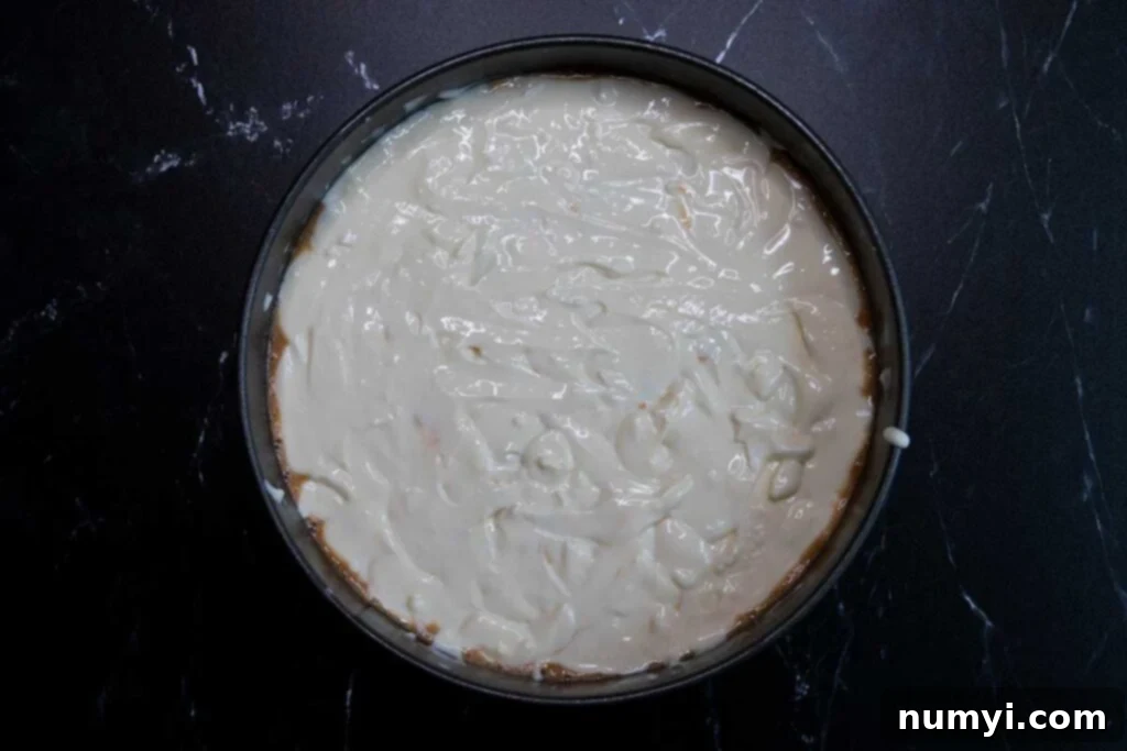 The final layer of cheesecake batter carefully spread over the carrot cake, creating a smooth, even surface before baking.