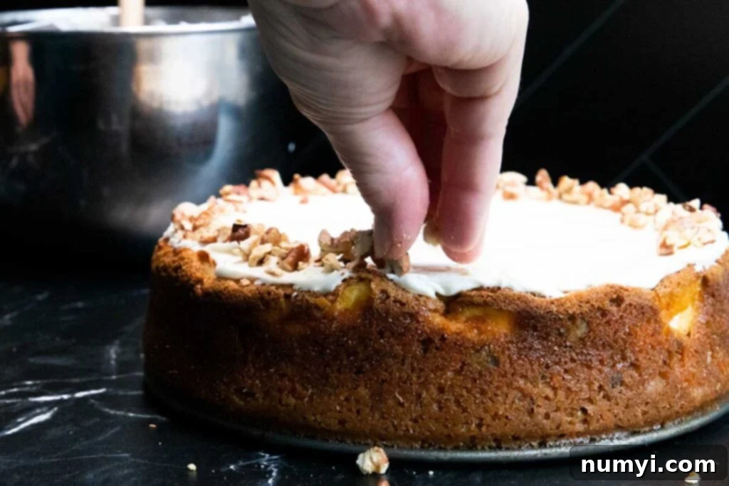 Chopped toasted pecans being sprinkled artfully over the cream cheese frosting on a carrot cake cheesecake, adding texture and garnish.