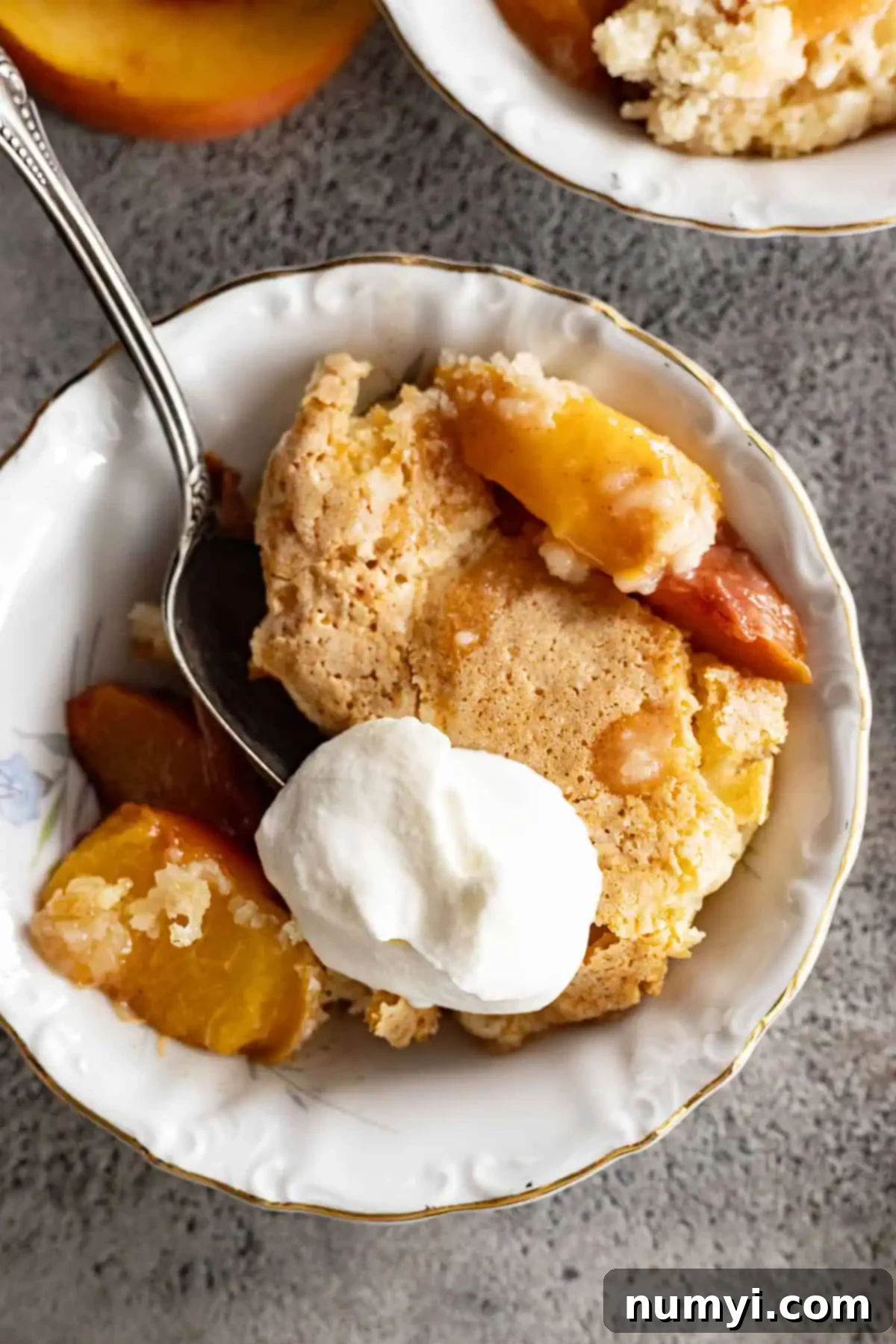 Overhead view of peach cobbler in a white bowl with whipped cream.