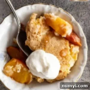 Overhead view of peach cobbler in a white bowl with whipped cream.