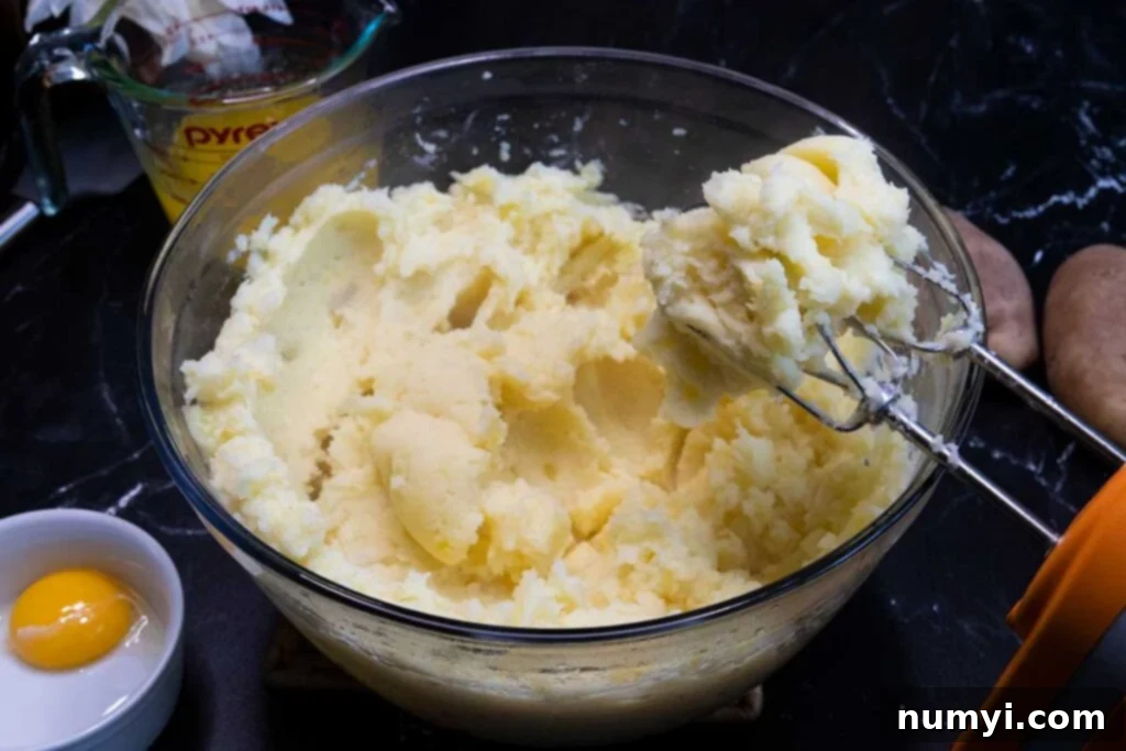 Potatoes being blended with a hand mixer in a large bowl.