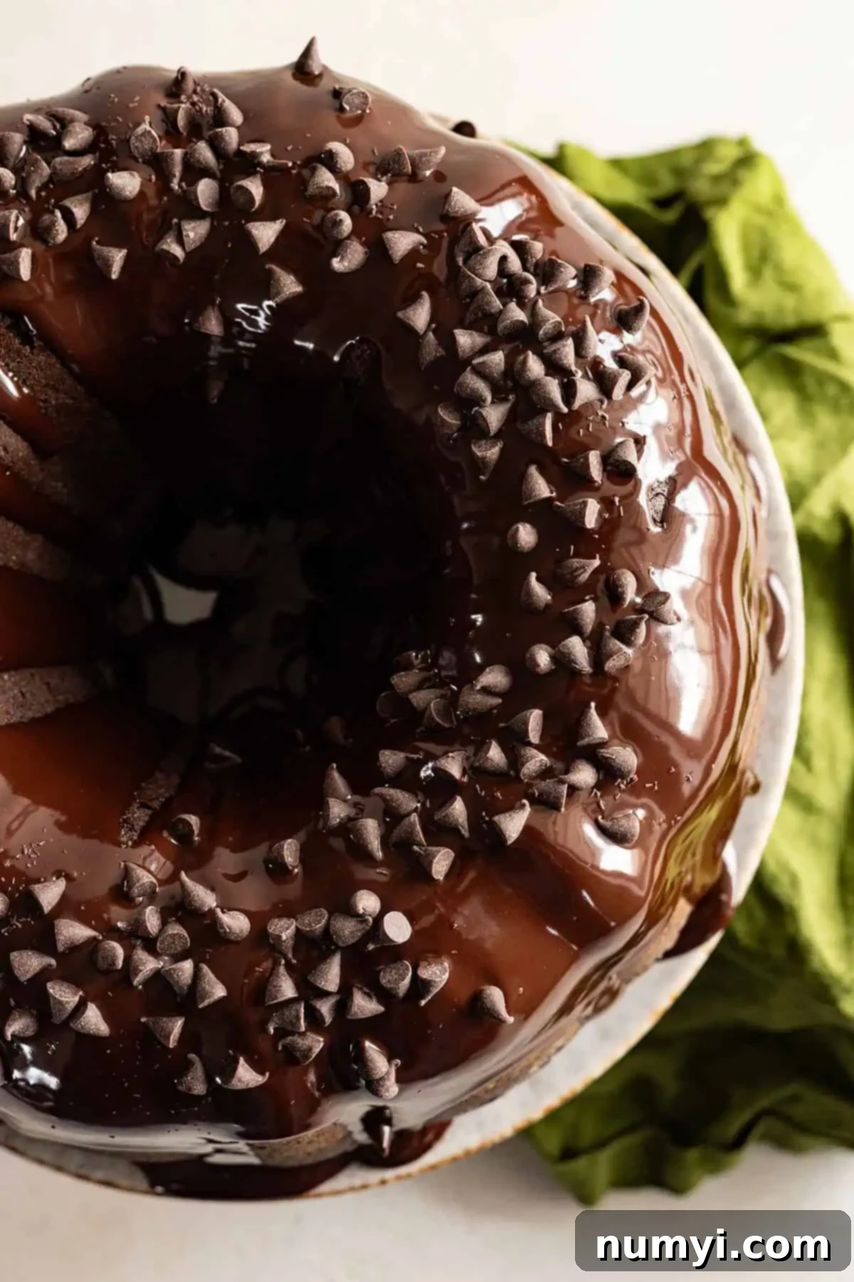A stunning Chocolate Zucchini Bundt Cake, generously glazed and sprinkled with chocolate chips, sitting on a cake stand.