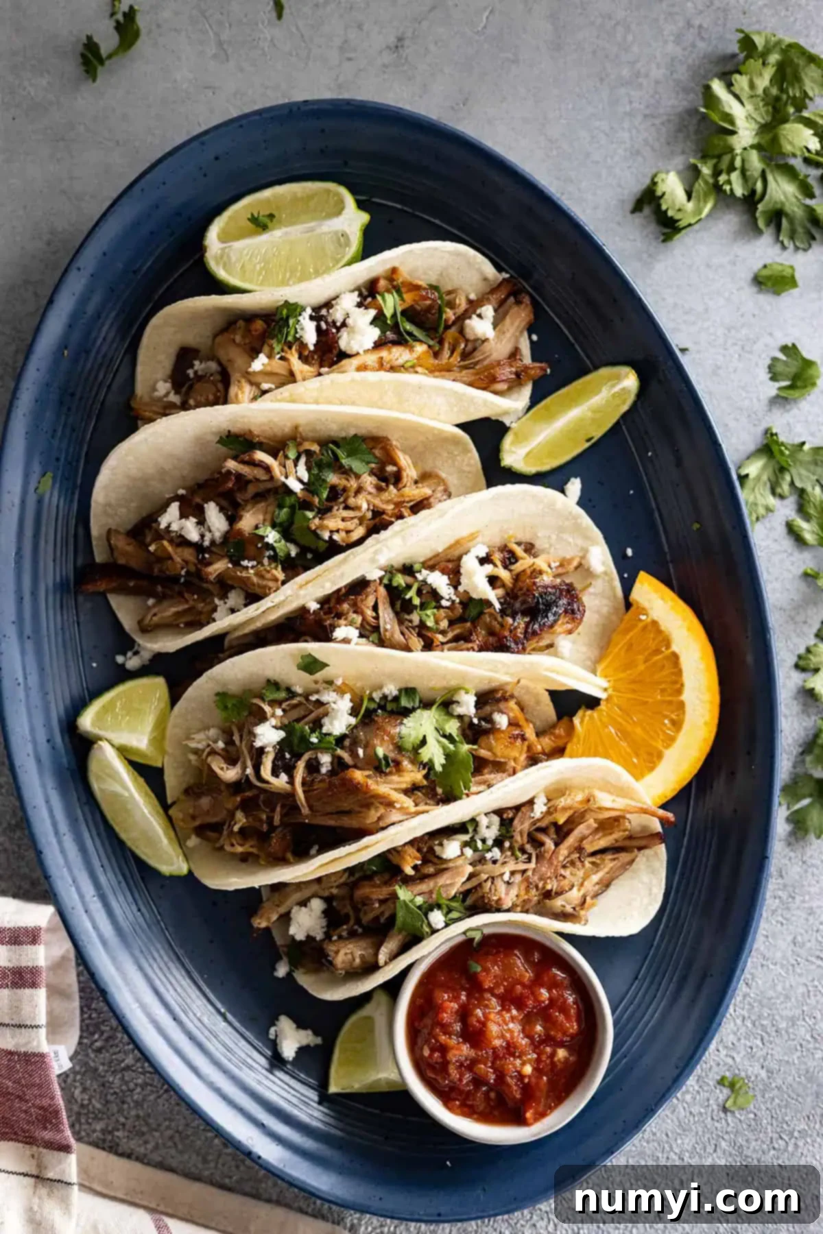 Overhead view of carnitas in tortillas all lined up on a blue plate. 