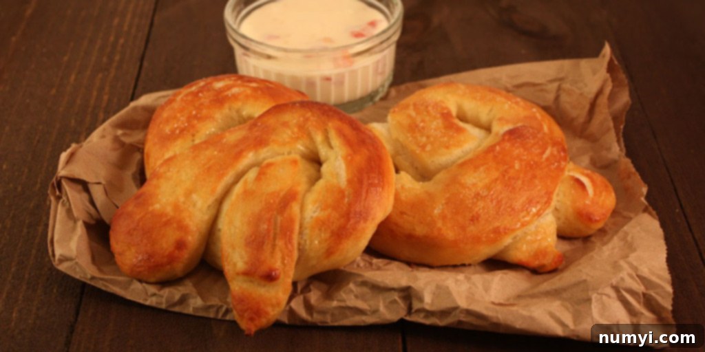 Freshly baked soft pretzels on brown paper with a ramekin of savory cheese dip, highlighting their golden-brown crust and inviting texture.