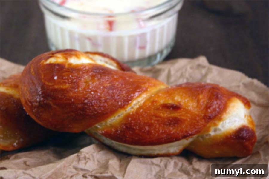 Close-up of freshly baked soft pretzels on brown paper, showing off their perfectly salted, golden crust, with a bowl of cheese dip in the background.