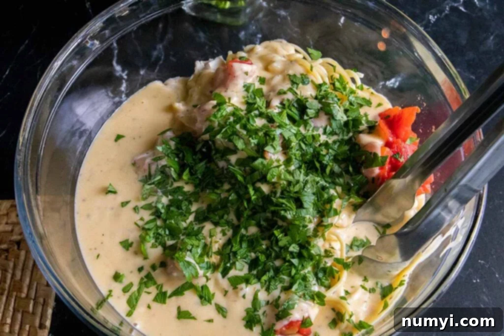 Creamy Chicken and Cheese Spaghetti 5 A large glass mixing bowl filled with cooked spaghetti, diced chicken, tomatoes, and parsley, awaiting the creamy cheese sauce.