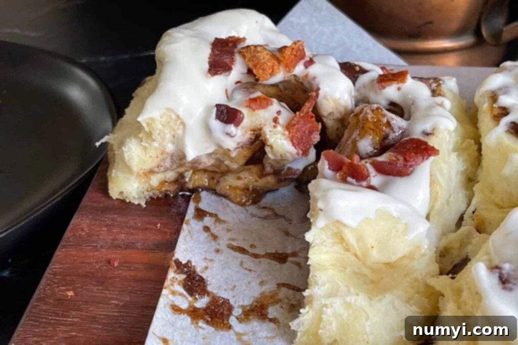 A close-up of a warm, gooey Maple Bacon Cinnamon Roll, cut in half to show the beautiful spiral.