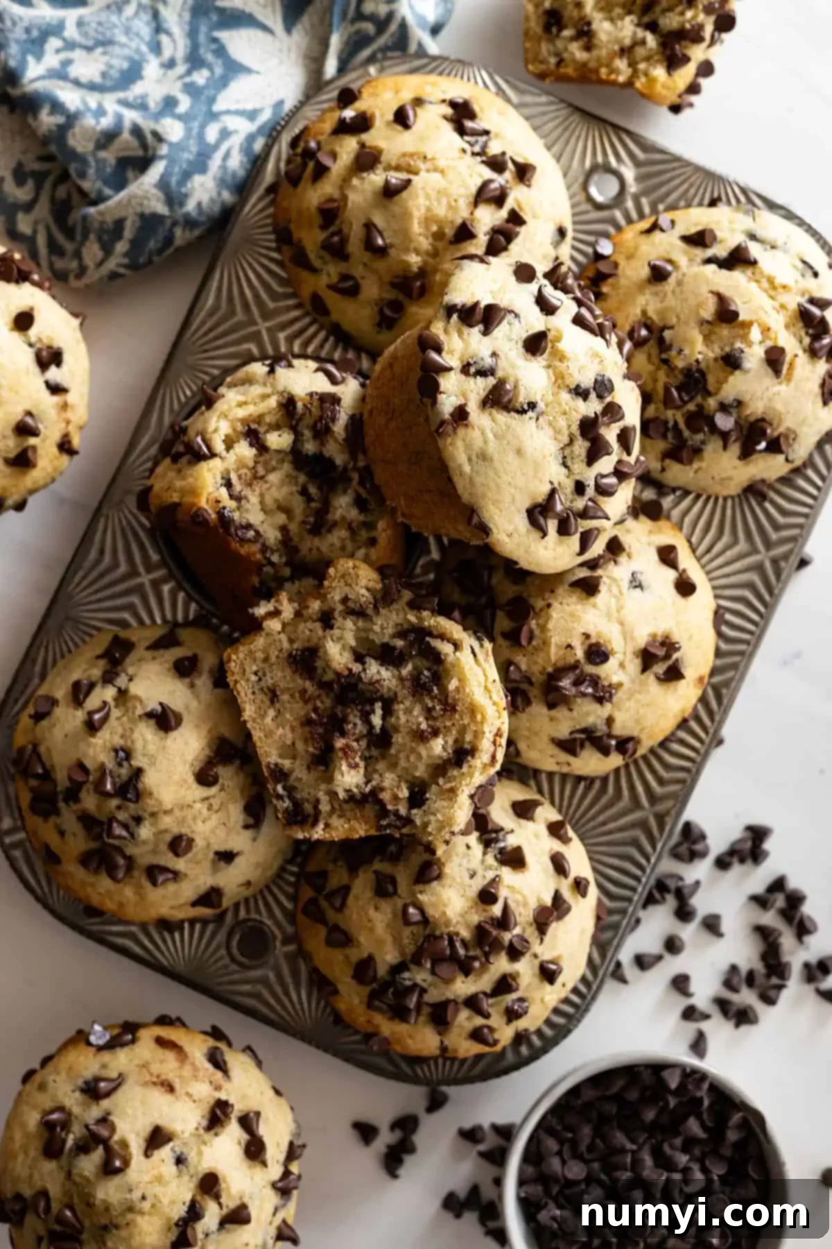 Overhead view of muffins piled in and around an antique muffin pan with chocolate chips scattered to the side. 