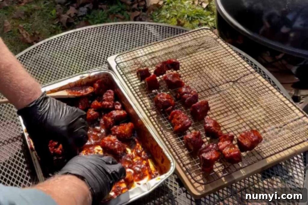 Ultimate Pork Butt Burnt Ends 14 Sauced pork butt burnt ends being carefully transferred from a pan to a Bradley rack, ready for the final step of tacking up in the smoker.