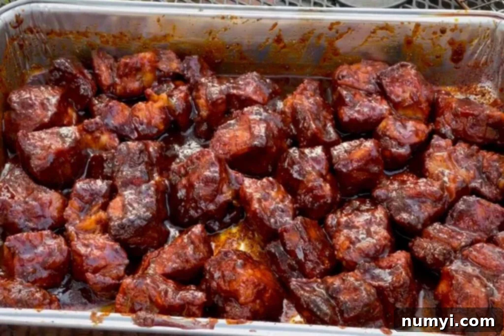 Ultimate Pork Butt Burnt Ends 15 A generous serving of glistening pork butt burnt ends on a black plate, ready to be enjoyed, showcasing their perfect glaze and tender appearance.