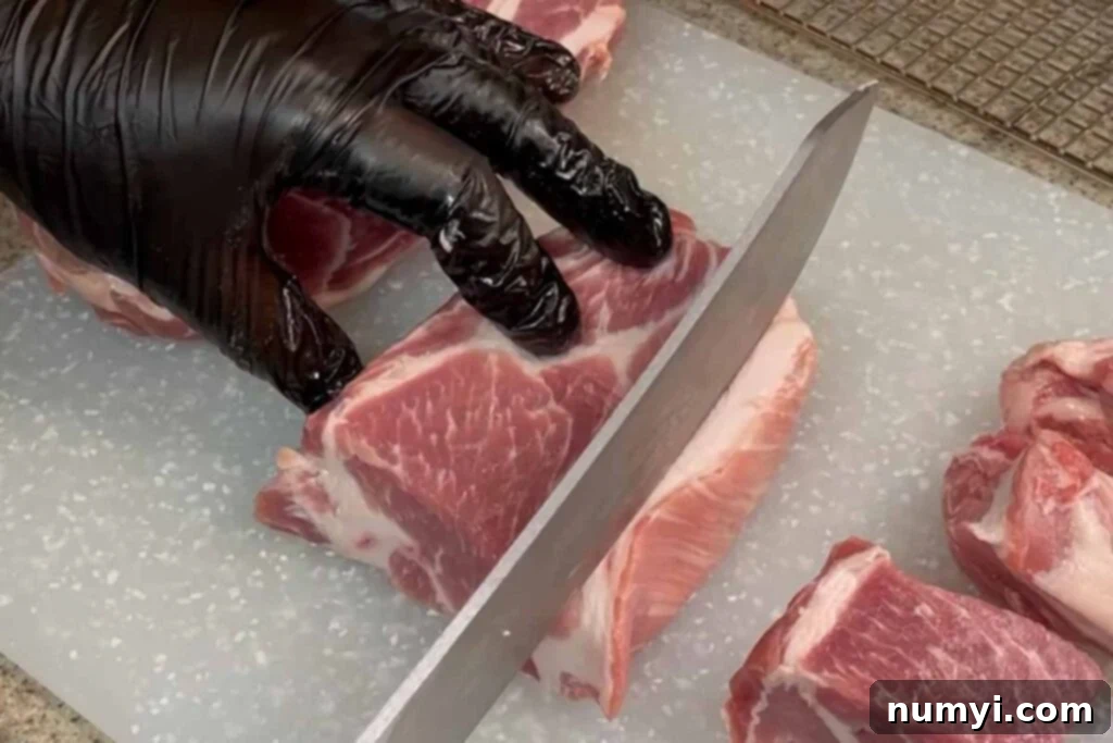 Ultimate Pork Butt Burnt Ends 4 A sharp knife carefully trimming excess fat from a piece of raw pork butt, essential for better smoke penetration and bark formation.