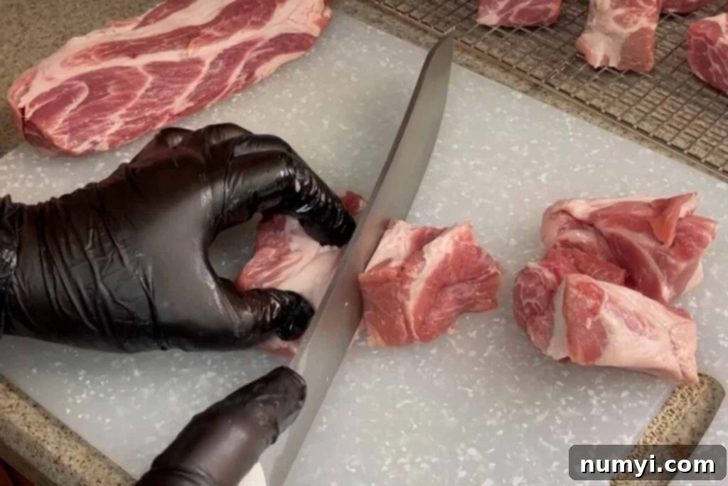Ultimate Pork Butt Burnt Ends 5 Hands expertly cutting a pork butt into uniform 1½ inch cubes on a cutting board, preparing them for the smoking process.
