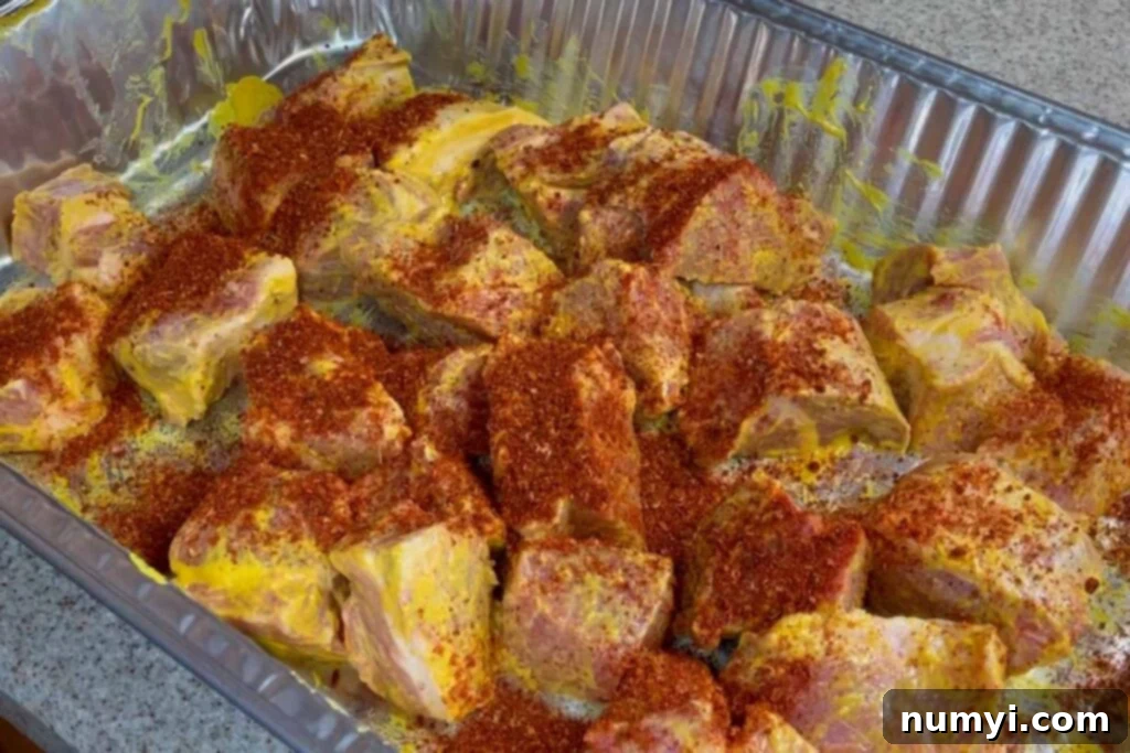 Ultimate Pork Butt Burnt Ends 7 Pork butt cubes evenly coated with a dry rub in a mixing bowl, showing the rich, dark color of the seasoning.