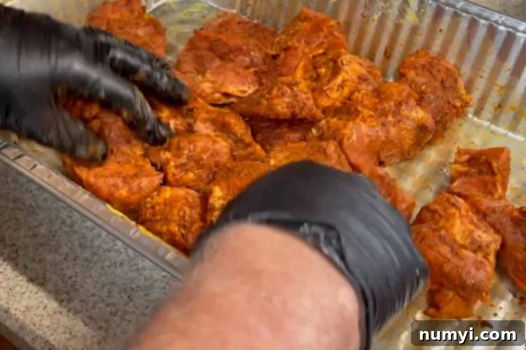 Ultimate Pork Butt Burnt Ends 8 A gloved hand tossing pork butt cubes seasoned with dry rub, ensuring every piece is uniformly covered before smoking.