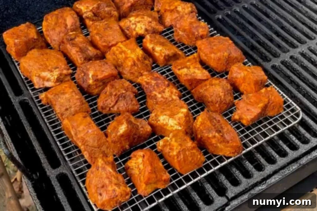 Ultimate Pork Butt Burnt Ends 10 Pork butt burnt ends cubes smoking on a rack inside a barbecue smoker, developing a deep smoky color and rich bark.